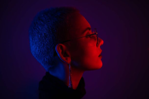 Portrait of beautiful young woman with short hair wearing glasses in neon light - Foto, Imagen