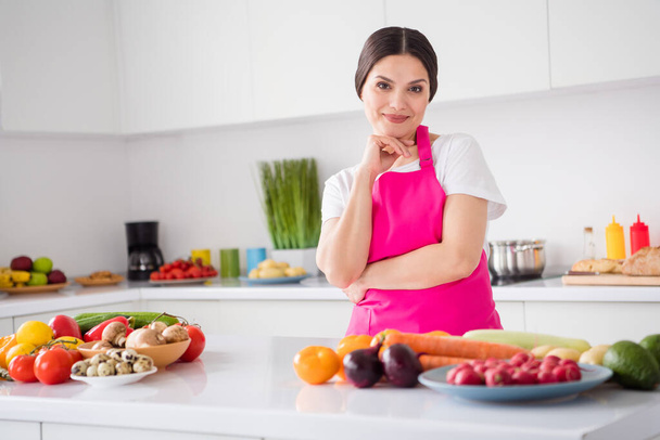 Photo of adorable thoughtful young lady wear pink apron hand chin cooking dinner smiling indoors room home house - 写真・画像