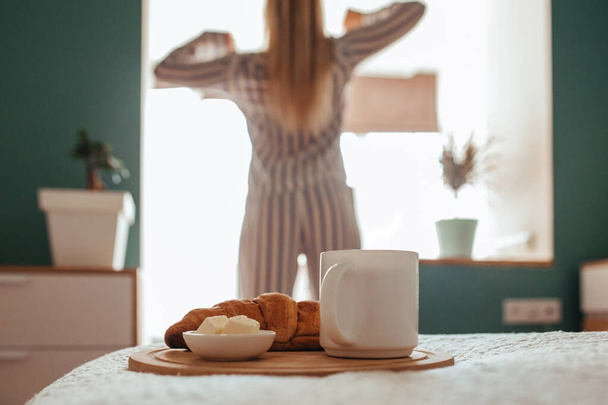 croissant and coffee in the foreground on the back of a girl in pajamas. breakfast concept - Photo, Image