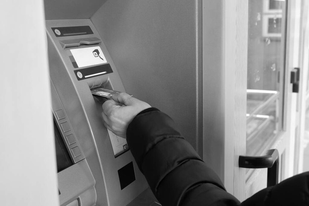 Ένα αντρικό χέρι εισάγει μια πιστωτική κάρτα σε ένα μηχάνημα ΑΤΜ. Ασπρόμαυρη εικόνα. - Φωτογραφία, εικόνα