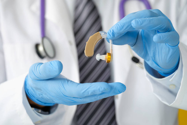 Hals-Nasen-Ohren-Arzt hält Hörgerät mit Gummihandschuhen in Nahaufnahme - Foto, Bild