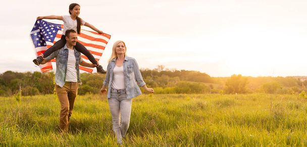 Gün batımında tarlada Amerikan bayrağı taşıyan güzel bir aile. Bağımsızlık Günü, 4 Temmuz. - Fotoğraf, Görsel