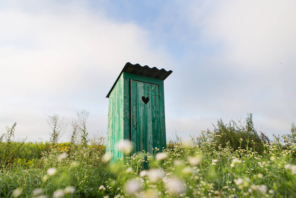 Toilettes anciennes. Une toilette verte rustique extérieure avec un cœur découpé sur la porte. Toilettes dans un champ de fleurs - Photo, image