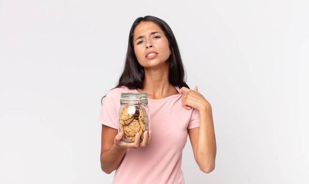 young hispanic woman feeling stressed, anxious, tired and frustrated and holding a cookies glass bottle - 写真・画像