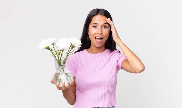 young hispanic woman looking happy, astonished and surprised holding decorative flowers - Foto, afbeelding