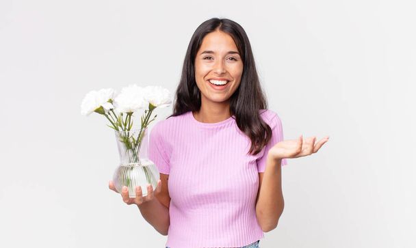 young hispanic woman feeling happy, surprised realizing a solution or idea holding decorative flowers - Valokuva, kuva