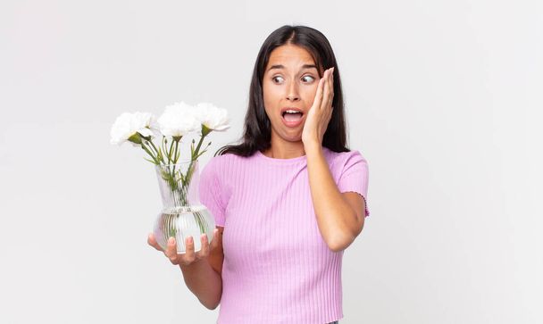 young hispanic woman feeling happy, excited and surprised holding decorative flowers - Photo, Image