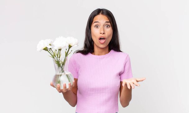 young hispanic woman feeling extremely shocked and surprised holding decorative flowers - Fotografie, Obrázek