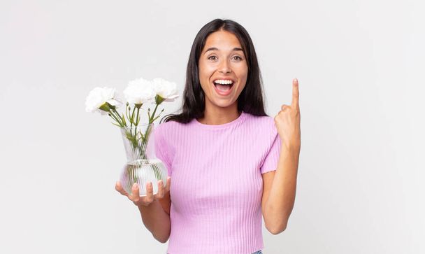 young hispanic woman feeling like a happy and excited genius after realizing an idea holding decorative flowers - Fotó, kép
