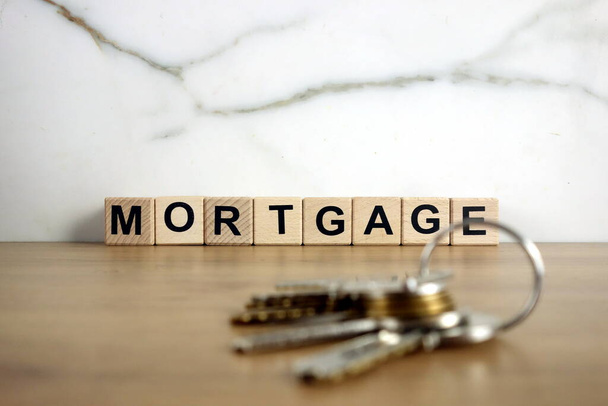 Hypothekenwort aus Holzklötzen und Hausschlüsseln. Immobilien, Vermietung, Investition oder Umzugskonzept - Foto, Bild