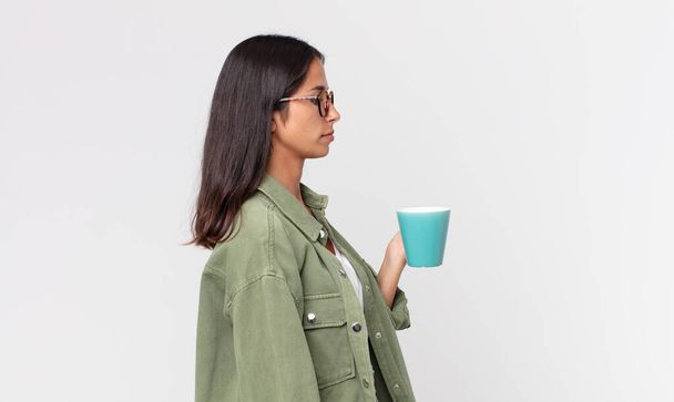 young hispanic woman on profile view thinking, imagining or daydreaming and holding a coffee mug - Foto, Bild