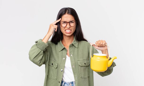 young hispanic woman feeling confused and puzzled, showing you are insane and holding a tea pot - Foto, Imagen