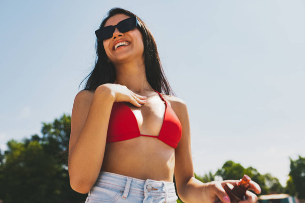 Молодая улыбающаяся женщина, девушка в солнечных очках, отдыхающая, загорающая на открытом воздухе в яркий летний день. - Фото, изображение