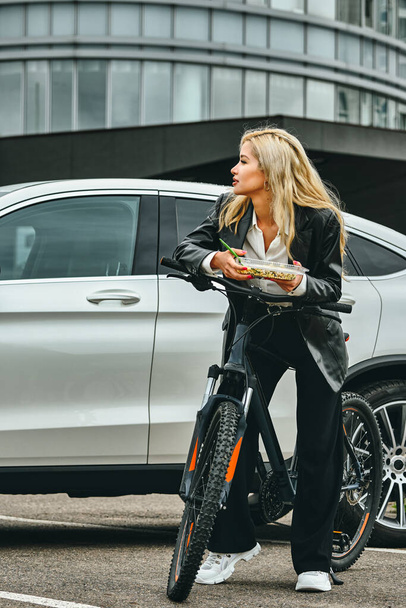 business woman portrait on a bike. girl having lunch on the street - Фото, изображение