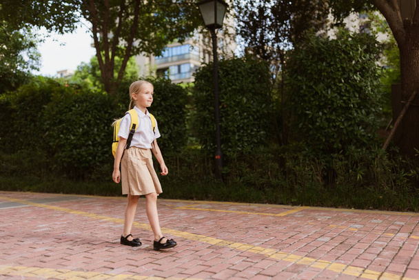 Schoolgirl back to school after summer vacations. Child in uniform smiling early morning outdoor.  - Фото, изображение
