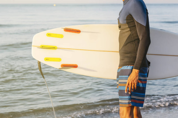 Профільний знімок молодого чоловіка, що стоїть з дошкою для серфінгу на пляжі
. - Фото, зображення