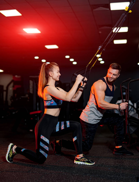 Sporty couple workout in the gym. Young athletic personal trainer helping his client. - Valokuva, kuva