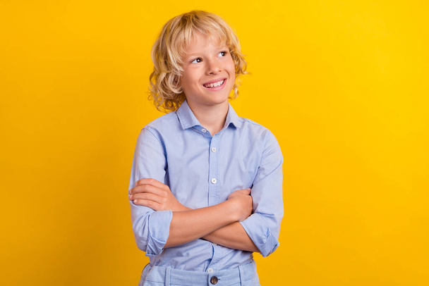 Photo of confident sweet schoolboy wear blue shirt arms crossed looking empty space smiling isolated yellow color background - Фото, изображение