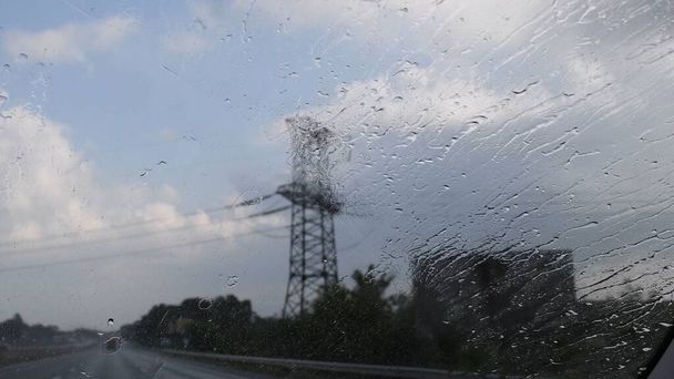 Автомобільне вітрове скло з бризками дощів і розмитою вежею передачі силует позаду
 - Фото, зображення