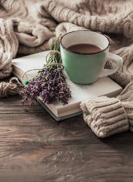 Dobré ráno. Šálek kávy na otevřené knize na dřevěném stole a teplý svetr na pozadí kytice levandule. Koncept zátiší. Kopírovat prostor. - Fotografie, Obrázek