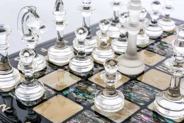 Transparent different glass chess pieces figures standing on pearl board in white. Glossy and matte set of shapes. game concept of confrontation. - Photo, Image