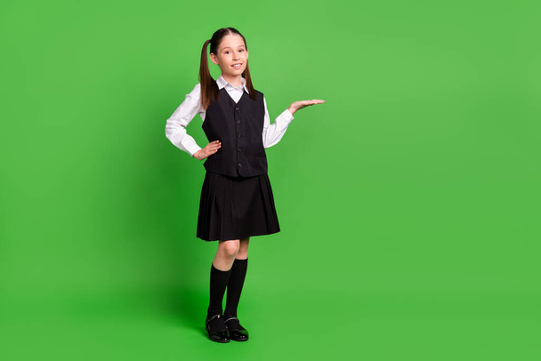 Photo of shiny sweet school girl wear black white uniform standing smiling holding arm empty space isolated green color background - 写真・画像