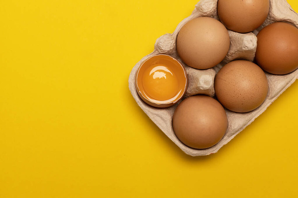 Świeże wielkanocne brązowe jaja kurze i jedno rozbite jajko z żółtkiem w eko koszyku na żółtym tle - Zdjęcie, obraz