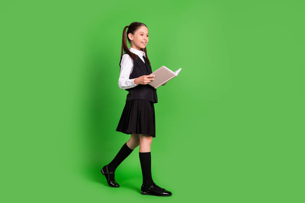 Full length body size profile side view of attractive cheerful girl reading book going isolated over bright green color background - Foto, Imagem