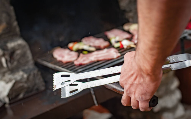 Man cooking meat on barbecue grill at bbq party in summer garden. Food, people and family time concept - Photo, image