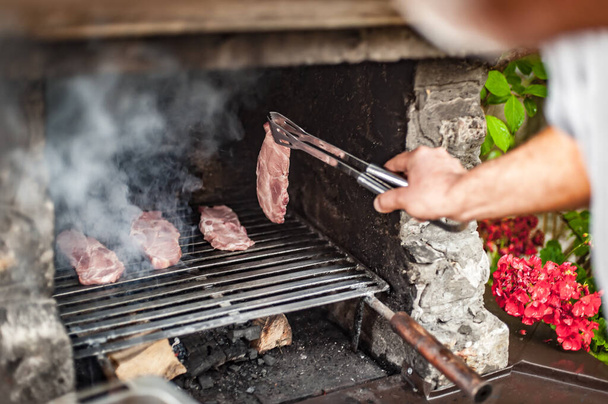 Man cooking meat on barbecue grill at bbq party in summer garden. Food, people and family time concept - 写真・画像