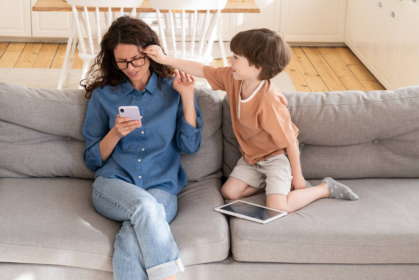 Aktivní znuděný malý syn rozptýlit mladá matka businesswoman práce na online na smartphone z domova - Fotografie, Obrázek