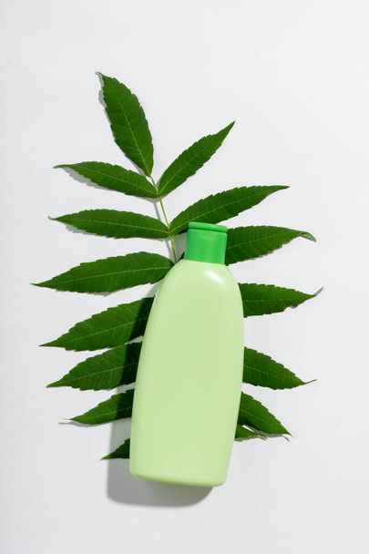 Cosmetic product in green tube with empty space for branding label. Natural cosmetics for skin and hair care. Shampoo or lotion with leaf shadow on white background - Foto, immagini