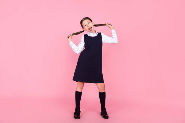 Full length body size photo schoolgirl showing tongue grimacing keeping tails isolated pastel pink color background - 写真・画像