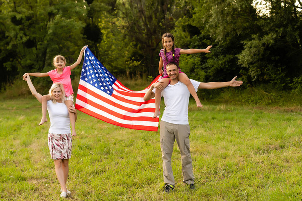 Счастливая семья с американским флагом на пшеничном поле на закате. День независимости, 4 июля. - Фото, изображение