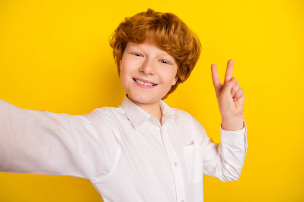 Photo of young smiling good mood handsome boy take selfie showing v-sign isolated on yellow color background - Photo, Image