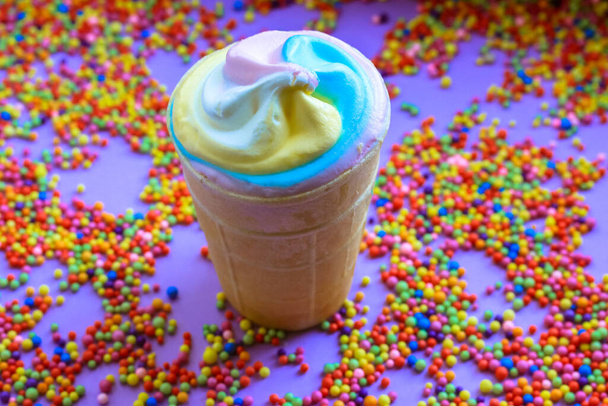 Πολύχρωμο δροσερό παγωτό σε ένα κύπελλο βάφλα σε ένα πολύχρωμο χάντρες δημιουργικό υπόβαθρο επίπεδη. Μοντέρνα χρώματα του καλοκαιριού 2021 - παστέλ μπλε, ροζ, κίτρινο. Γλυκό σνακ με πολλές θερμίδες. Έννοια θερινών τροφίμων. - Φωτογραφία, εικόνα