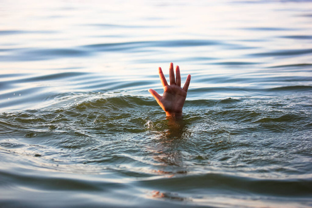 Ein Mann ertrinkt im Wasser. Eine Hand lugt unter dem Wasser hervor. Ein Ertrinkender braucht Hilfe, Rettung. Ein Risiko, eine Gefahr für das Leben im Meer, Fluss, Ozean, Teich. Tod, SOS-Konzept. Ertrinkungsopfer - Foto, Bild