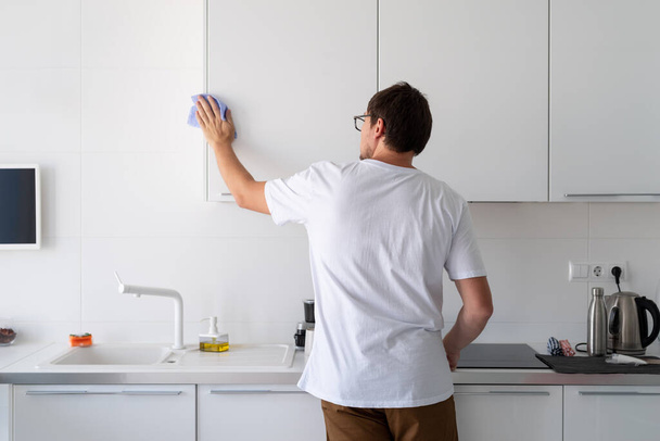Καθαρισμός και απολύμανση. Άνδρας σε λευκό πουκάμισο καθαρισμού στην κουζίνα - Φωτογραφία, εικόνα