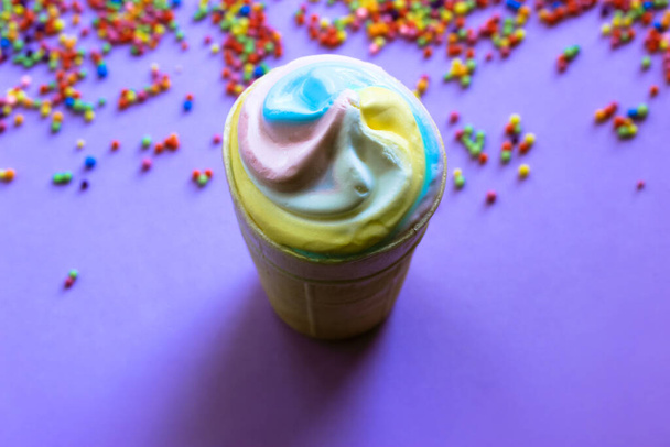 カラフルな色のビーズの創造的な背景にワッフルカップでカラフルなクールなアイスクリームをフラット。2021年夏の流行の色-パステルブルー、ピンク、黄色。高カロリーの甘いスナック。夏の食のコンセプト. - 写真・画像