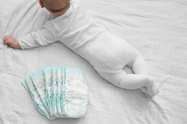 Baby met een stapel luiers op een wit bed. Gevoelige babyhuid. Pasgeboren baby - Foto, afbeelding
