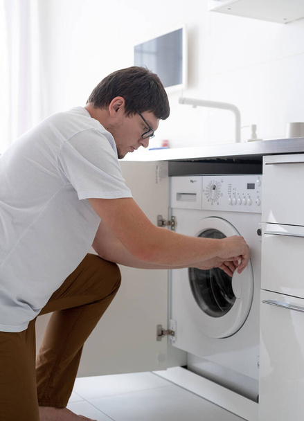 Jovem usando máquina de lavar roupa no dia da lavanderia em casa - Foto, Imagem