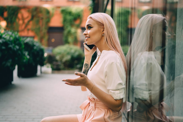 Pink haired female teenager enjoying international smartphone call conversation during resting time in city, carefree hipster girl 20 years old connecting roaming internet for making cellphone talking - Фото, зображення