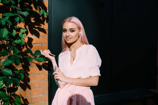 Half length portrait of happy female millennial with colored pink hair smiling at camera during leisure in sunny city, pretty Caucasian youngster with smartphone device in hand posing outdoors - Foto, Imagen