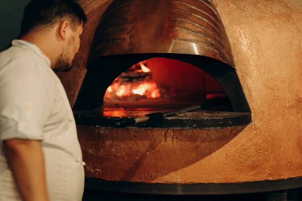 Le chef prépare une pizza dans un four à bois. Cuisiner une pizza. Le cuisinier met la pizza au four. Délicieuse pizza chaude du four. - Photo, image