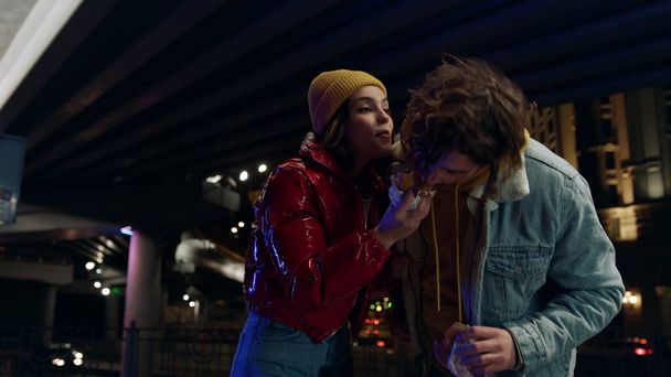 Feliz pareja besándose en la calle de la ciudad. Hombre mordiendo a la mujer hamburguesa al aire libre. - Foto, Imagen