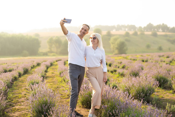 Usmívající se mladý pár objímající levandulové pole, držící se za ruce, kráčející. - Fotografie, Obrázek