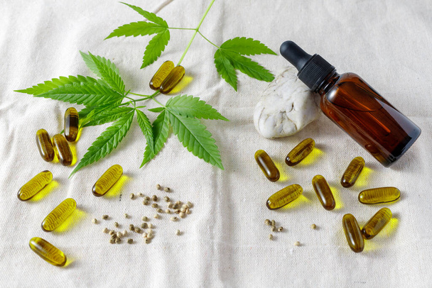 CBD oil capsules from sativa seeds, medical hemp oil  glass bottle, leaves an seeds on canvas fabric  background. Cannabis growing  and food supplements concept - Photo, Image