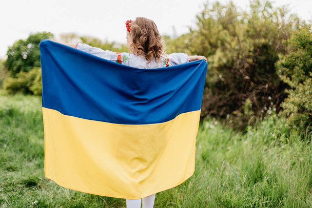 Ukraines Independence Flag Day. Constitution day. Ukrainian child girl in embroidered shirt vyshyvanka with yellow and blue flag of Ukraine in field. flag symbols of Ukraine. Kyiv, Kiev day - Foto, Imagem