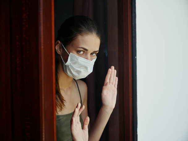 γυναίκα με ιατρική μάσκα κοιτάζοντας έξω από το παράθυρο αποκλεισμού δυσαρέσκεια, κλείδωμα - Φωτογραφία, εικόνα