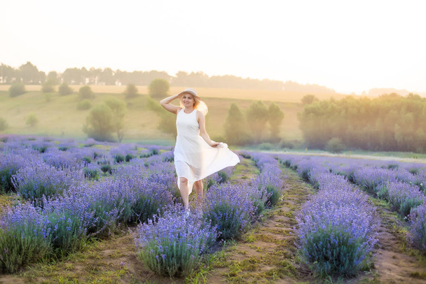 Beautiful young woman walking the field of lavender. Fashion outfit dress, straw hat. - Foto, Bild